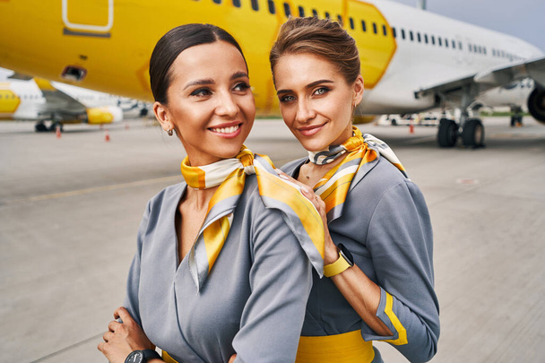 Две симпатичные стюардессы в форме возле приземлившегося самолета - Фото, изображение