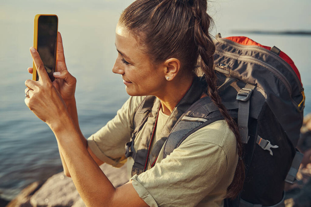 Backpacker taking a picture of lake view on smartphone - Foto, imagen