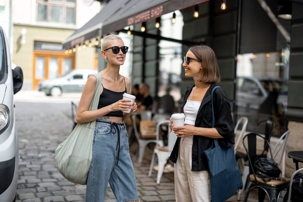 Elegante pareja femenina de pie junto con un café tazas al aire libre - Foto, Imagen