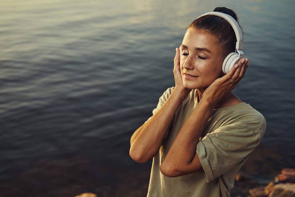 Female getting lost in music at lakeside - Foto, Bild