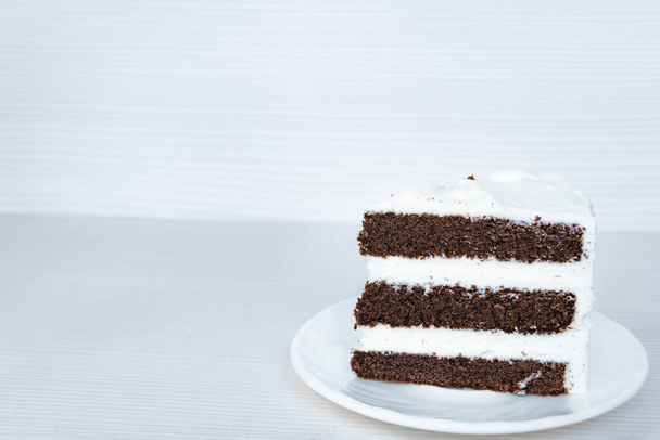 Μια φέτα κέικ σοκολάτας σφουγγάρι με κρέμα βουτύρου βρίσκεται στα δεξιά. - Φωτογραφία, εικόνα