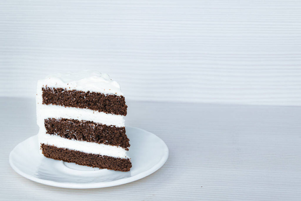 The slice of chocolate sponge cake with butter cream is located on the left. White background. - Foto, Imagem