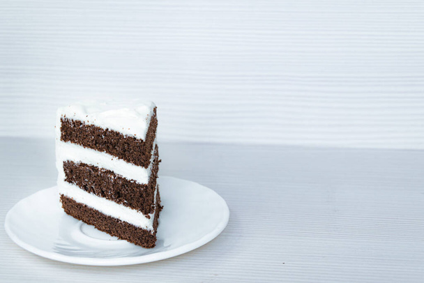 A slice of chocolate sponge cake with butter cream is located on the left. White background. - Foto, Bild