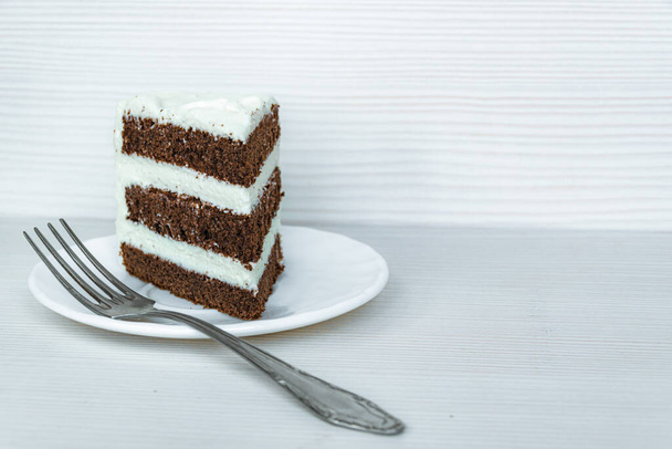 A fork and a slice of chocolate sponge cake with butter cream are located on the left. White background. - Foto, immagini