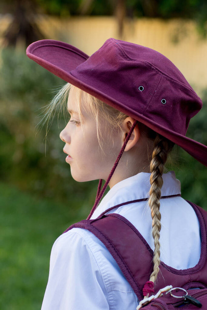 Ein Mädchen in Schuluniform, weißem Hemd, kastanienbraunem Rucksack und kastanienbraunem Hut. Rückkehr in Klassenzimmer nach COVID-19-Ausbruch in Australien - Foto, Bild