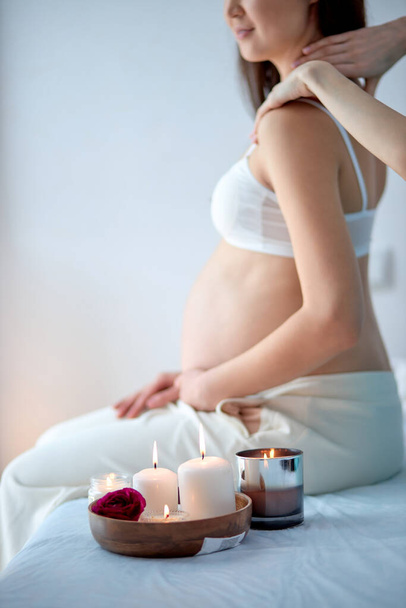 Pregnant woman receiving back massage from masseur in spa cabinet, sit with candles - Фото, изображение