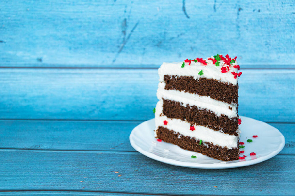 A piece of chocolate sponge cake with a layer of butter cream located on the right. Blue background. Red-green dusting. Close-up. - Foto, Bild
