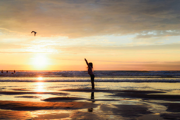 子供はビーチで遊んでいる若い女の子は日没時に海の中で水を撒いている - 写真・画像