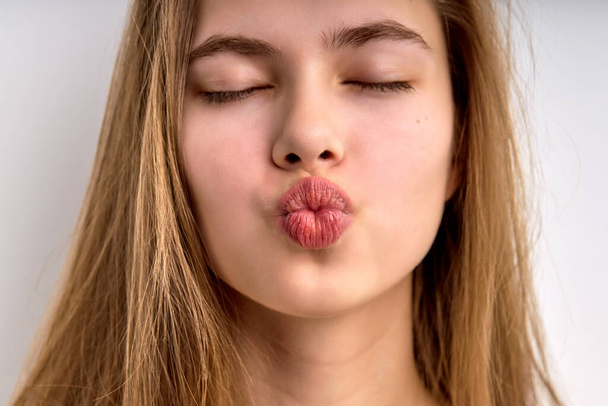 Close-up portrait of young girl kissing with eyes closed, isolated on white background - Valokuva, kuva