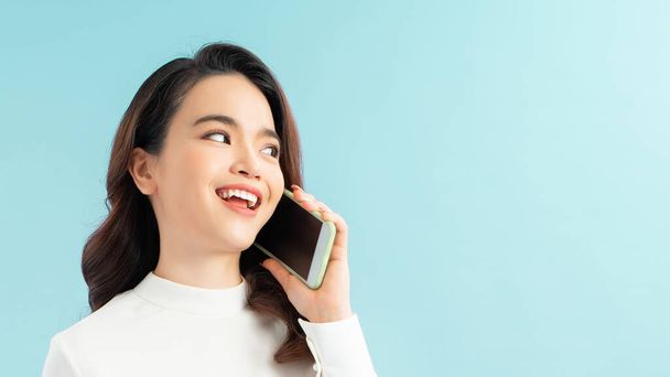 Retrato de una linda chica feliz en vestido hablando por teléfono móvil y riendo aislado sobre fondo azul - Foto, imagen