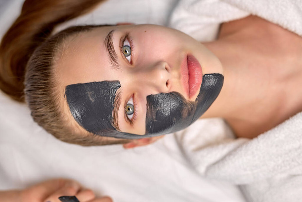 Top View On Good-looking Cute Female With Black Facial Mask on Half Of Face - Фото, изображение