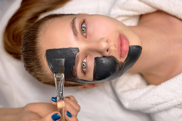 Top view on woman with black cosmetic facial mask lying on bed at spa. Face peeling - Foto, Imagen