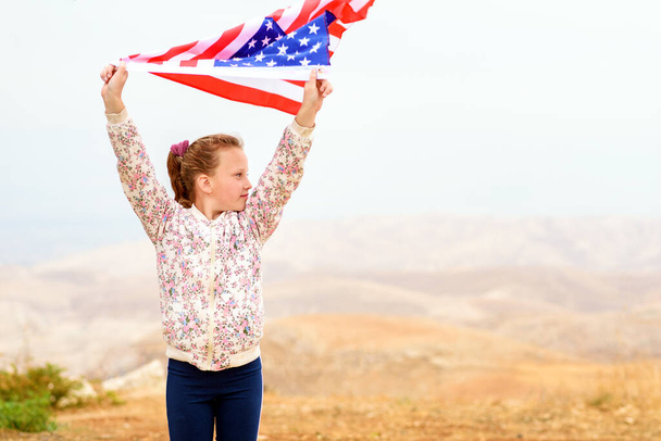 Pieni isänmaallinen onnellinen tyttö, jolla on Amerikan lippu heiluttamassa luontoa ulkona. USA juhlii 4. heinäkuuta. - Valokuva, kuva