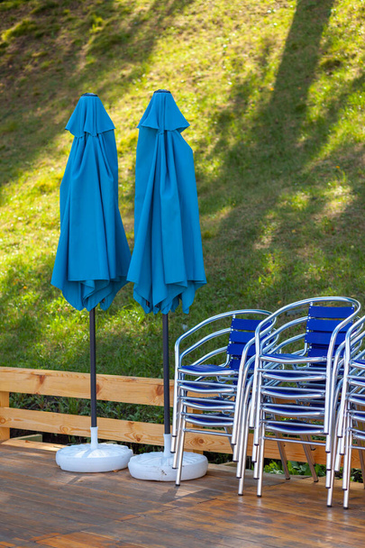 Sillas de metal apiladas en pilas, y al lado de un paraguas de playa en un restaurante callejero, cafetería o centro de recreación. Las sillas están en el suelo de madera. Los resorts están esperando turistas y visitantes - Foto, imagen