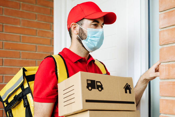 Delivery man wearing face mask ringing the house doorbell to deliver package - Фото, изображение