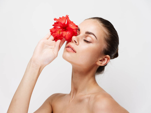 woman with red flower in front of eyes naked shoulders  - Foto, Imagen