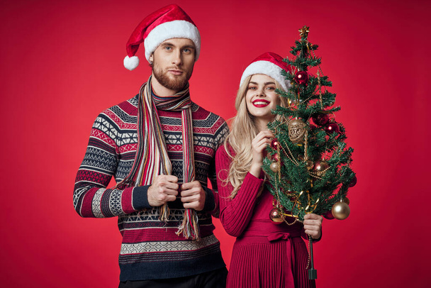 クリスマスツリーのおもちゃの隣に立つ男女ライフスタイル赤の背景 - 写真・画像