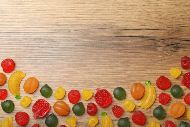 Delicious gummy fruit shaped candies on wooden table, flat lay. Space for text - Foto, Imagen