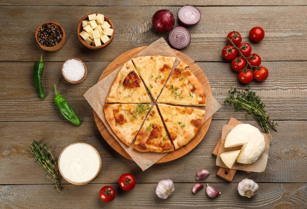 Delicious khachapuri with cheese, sauce, vegetables and spices on wooden table, flat lay - Foto, immagini