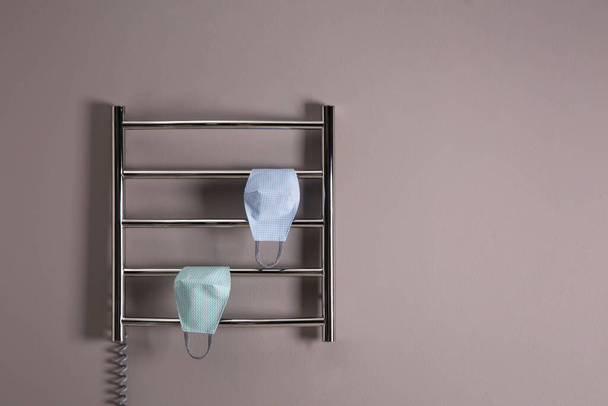 Modern heated towel rail with cloth face masks on grey wall. Space for text - Foto, Imagen