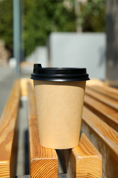 Takeaway cardboard coffee cup with plastic lid on wooden bench outdoors - Fotó, kép