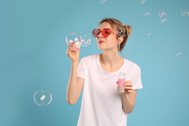 Young woman blowing soap bubbles on light blue background - Photo, Image
