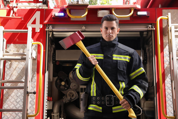 Portrait of firefighter in uniform with axe near fire truck outdoors - Fotografie, Obrázek