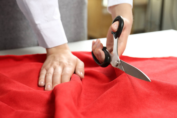 Seamstress cutting red fabric with scissors at workplace, closeup - Foto, Bild