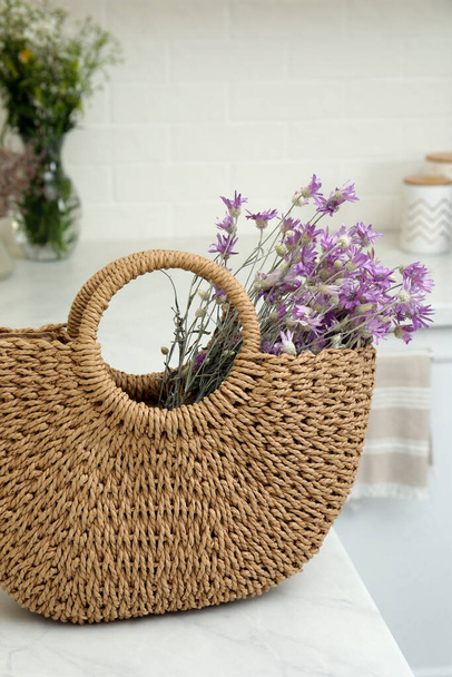Stylish beach bag with beautiful bouquet of wildflowers on white table in kitchen - Foto, Bild