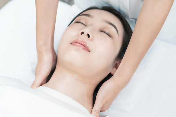 Aziatisch jong vrouw wiens hoofd wordt gemasseerd op een esthetische salon - Foto, afbeelding