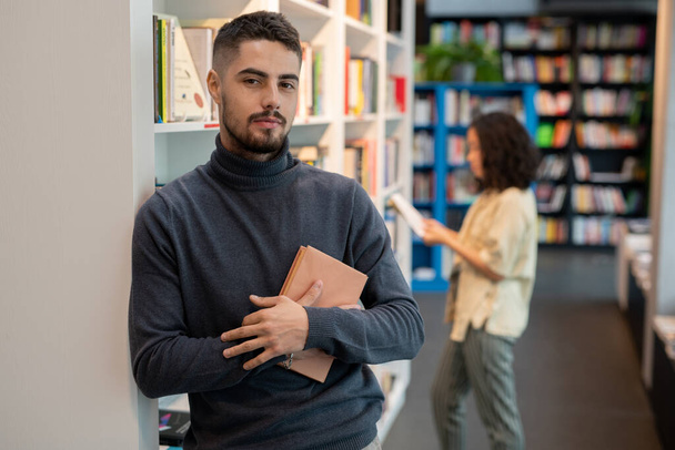 Bearded young man with book standing against female choosing literature - Photo, image