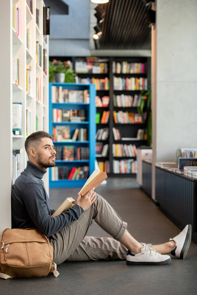 Νεαρός αφηρημένος άντρας με ανοιχτό βιβλίο κοιτάζοντας στην άκρη - Φωτογραφία, εικόνα