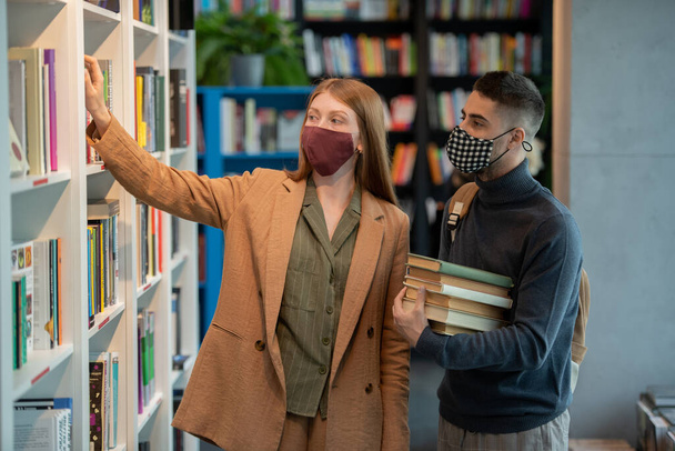 Small group of young students in masks choosing books - Фото, зображення