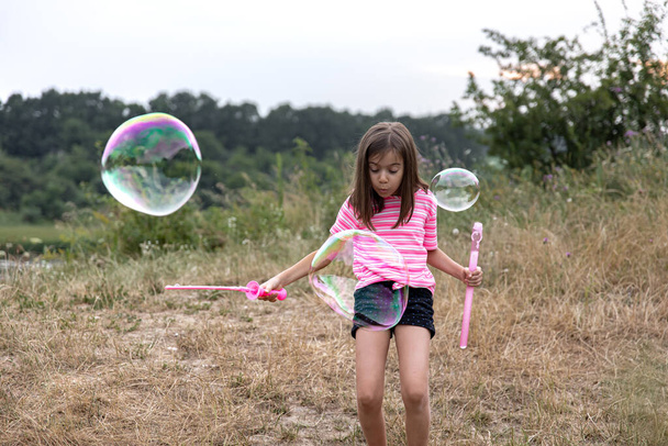 A pretty child girl launches huge soap bubbles in the background beautiful nature. - Foto, immagini
