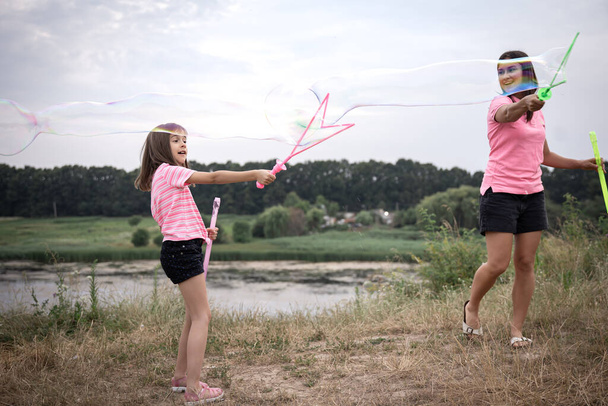 Eine junge Frau und ihre Tochter lassen im Hintergrund riesige Seifenblasen aufsteigen. - Foto, Bild