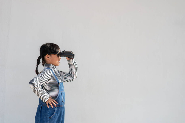 Little Asian girl looking through binoculars in white background. Explore and adventure concept. - Foto, Imagem