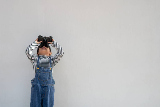 Little Asian girl looking through binoculars in white background. Explore and adventure concept. - Valokuva, kuva
