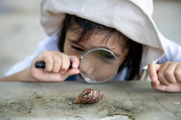 Szczęśliwa dziewczynka badająca naturę ze szkłem powiększającym i ślimakiem. Dobrze się bawi w ogrodzie. Koncepcja dziecka jest gotowa iść do szkoły.. - Zdjęcie, obraz