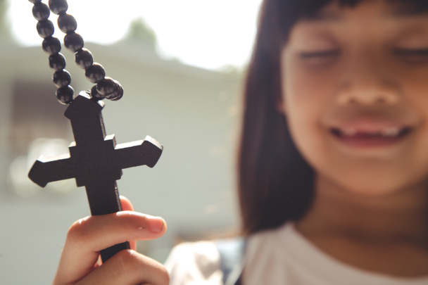 Маленька азійська дівчинка молиться, тримаючи хрест, християнське поняття.  - Фото, зображення