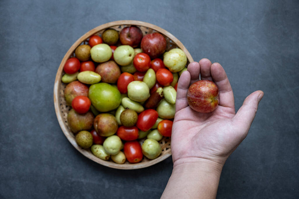 Uma variedade de frutas frescas, tâmaras, tomates cereja, Longan, ameixa, são definidos contra um fundo cinza escuro. - Foto, Imagem