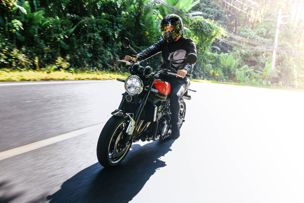 Hombre en un casco monta bicicleta en la carretera entre los trópicos de verano y mira a la cámara - Foto, Imagen