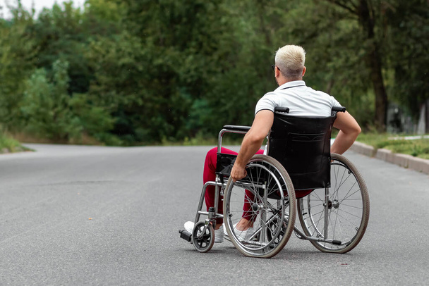 A disabled man sits in a wheelchair on the street. The concept of a wheelchair, disabled person, full life, paralyzed, disabled person, health care - Fotoğraf, Görsel