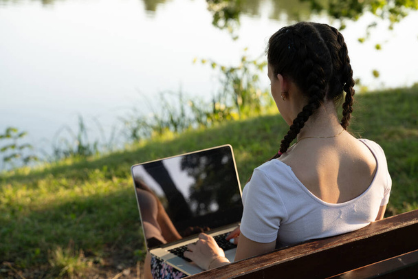 Δουλειά έξω. Μαθήτρια δουλεύει με λάπτοπ, τάμπλετ σε καλοκαιρινό πάρκο. Online τεχνολογία με γυναίκα εξωτερική. Απόδραση από την εξ αποστάσεως εκπαίδευση γραφείου - Φωτογραφία, εικόνα