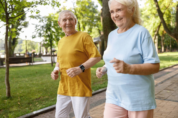 Älterer Mann läuft im Sommer mit hübscher sportlicher Frau im grünen Park entlang der Straße - Foto, Bild