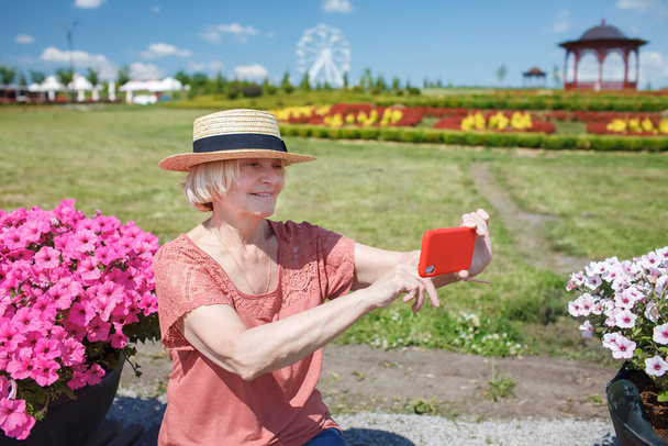 Šťastná seniorka se selfie na smartphone v parku během letních prázdnin, aktivní důchod - Fotografie, Obrázek
