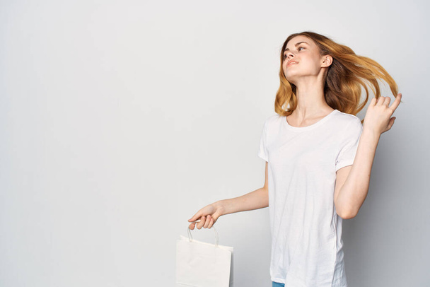 femme dans un t-shirt blanc avec un paquet dans ses mains gesticulant avec ses mains mockup - Photo, image