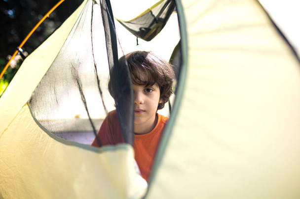 Un garçon regarde hors d'une tente, un portrait d'un enfant, un enfant voyage avec ses parents, un pique-nique dans la forêt, une randonnée dans les montagnes avec des enfants - Photo, image