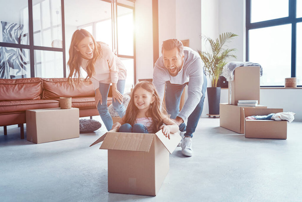 Happy young family smiling and unboxing their stuff while moving into a new apartment - Фото, зображення