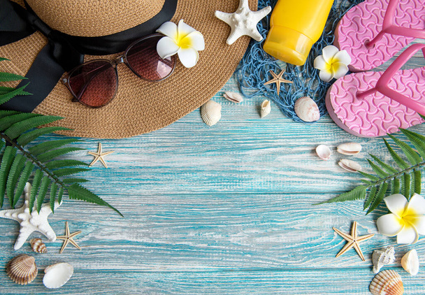 Koncept letních prázdnin. Slaměný klobouk a plážové doplňky s mušlemi a hvězdice na modrém dřevěném pozadí - Fotografie, Obrázek