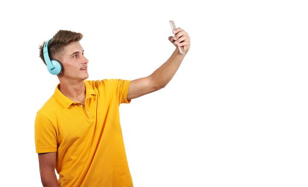 Fehér férfi sárga pólóban és fejhallgatóval, okostelefonos selfie-t készít. Tiszta fehér háttér, elszigetelt személy - Fotó, kép